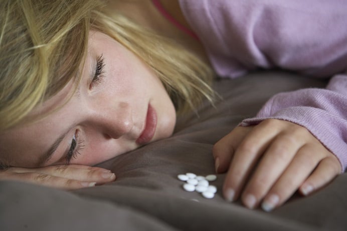 Depressed Teenage Girl Sitting In Bedroom With Pills