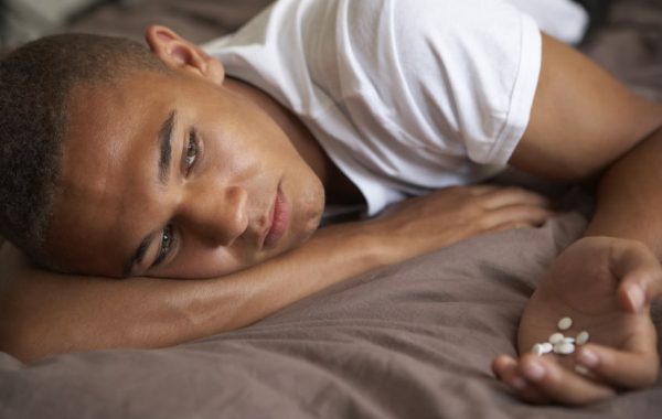 Depressed Teenage Boy Lying In Bedroom With Pills