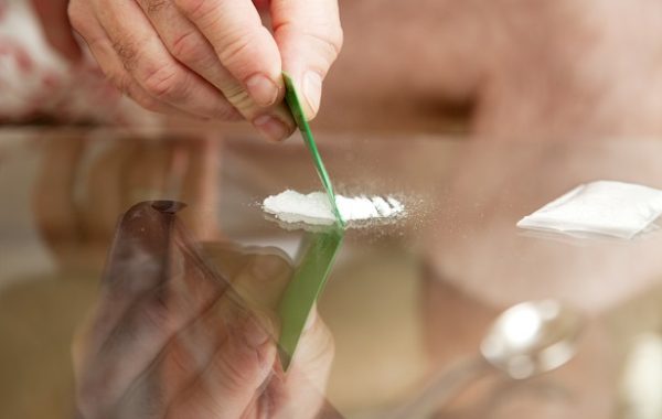 Closeup of a man's hand cutting cocaine on a glass table with a credit card.
